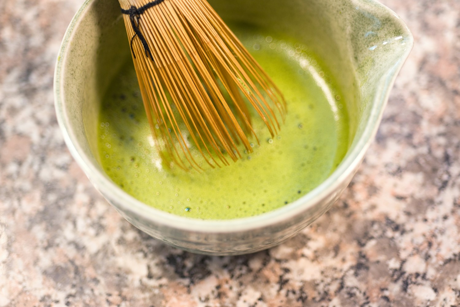 A bamboo whisk stirring matcha in a ceramic bowl